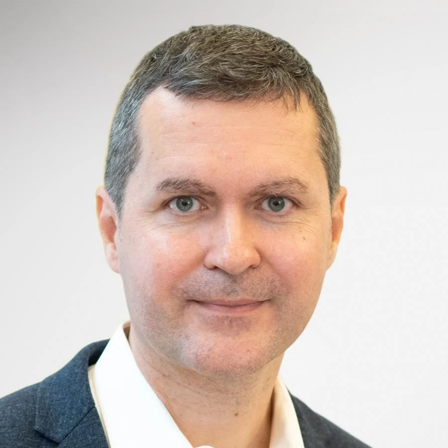 A man with short brown hair, white shirt, and dark blazer, smiling for AI-supported ID photos. A man with short brown hair, white shirt, and dark blazer, smiling for AI-supported ID photos.