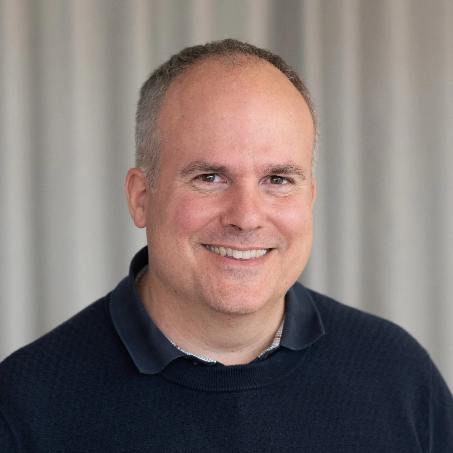 A smiling man with short gray hair in a dark sweater, standing in front of light curtains, using SCS Contact. A smiling man with short gray hair in a dark sweater, standing in front of light curtains, using SCS Contact.