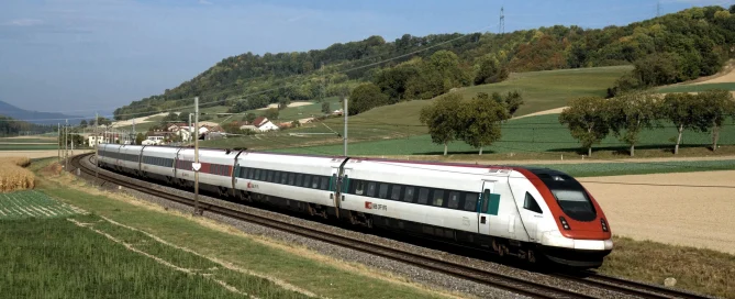A white and red high-speed train glides environmentally friendly through the green landscape under a blue sky.
