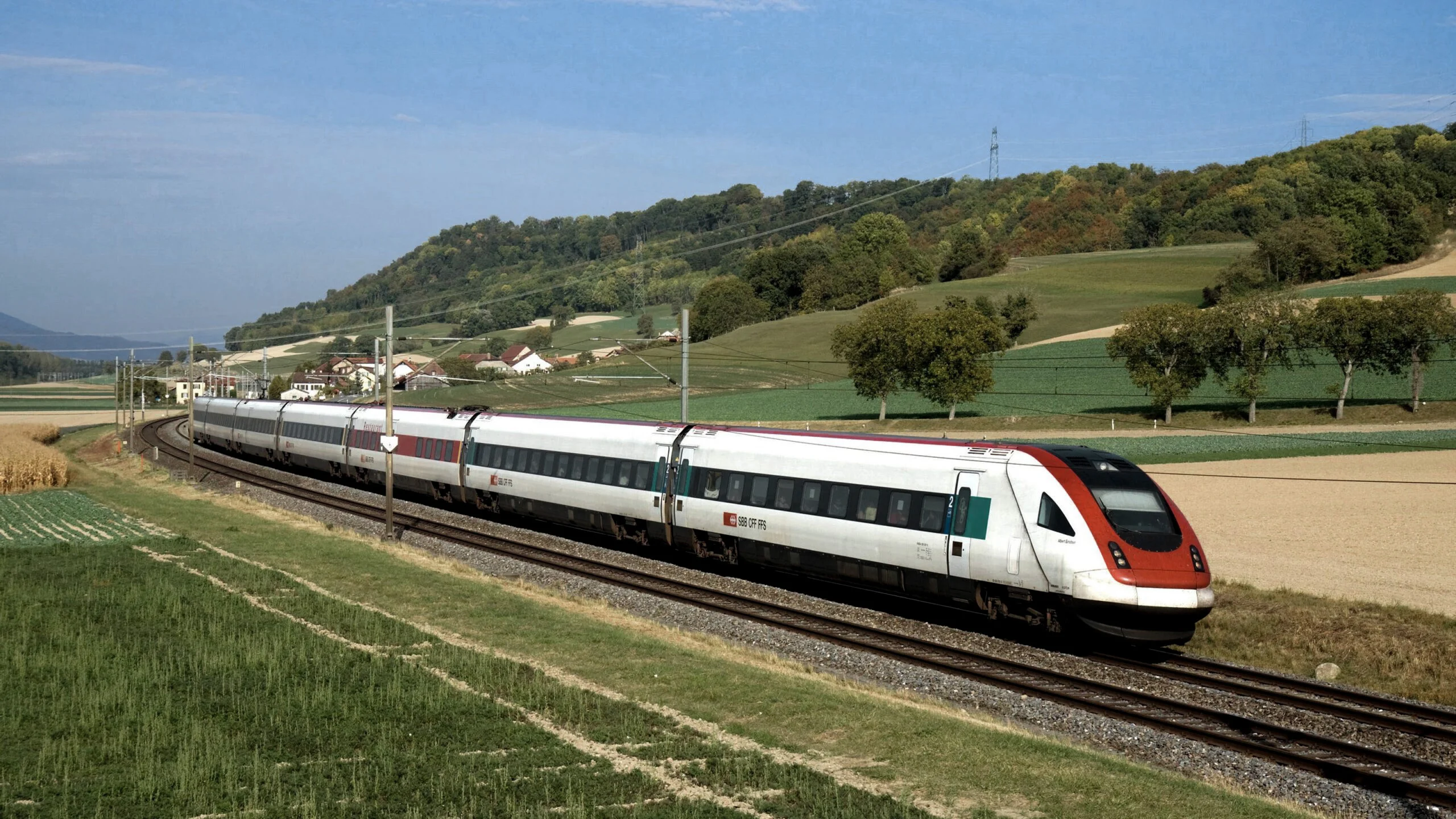 A white and red high-speed train glides environmentally friendly through the green landscape under a blue sky.