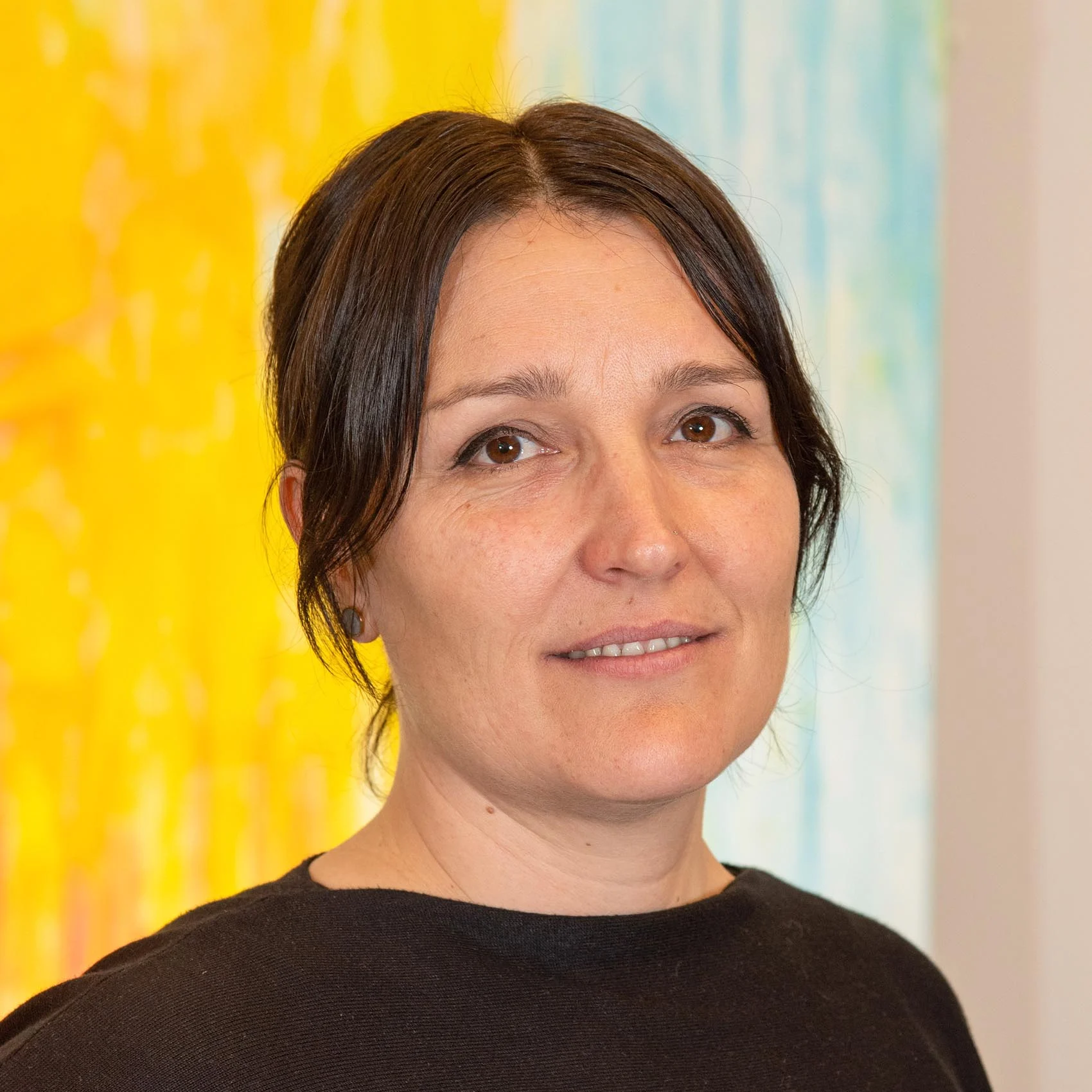 Woman with dark hair in a black top, standing in front of a colorful, abstract "SCS contact" background.