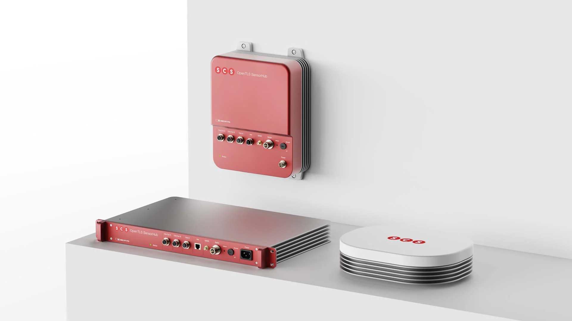 Three red and white SCS products – network devices – are displayed on a white shelf and wall. Three red and white SCS products – network devices – are displayed on a white shelf and wall.