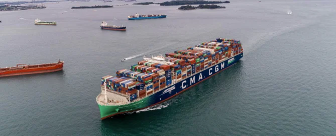 A large container ship labeled "CMA CGM" sails on the open sea, showcasing the industrial automation in its vicinity.