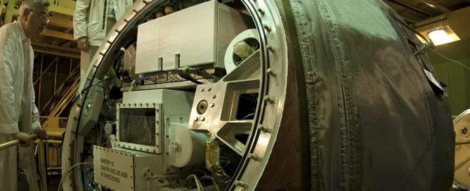 Two people inspecting a large, round, metallic embedded system in an industrial environment.