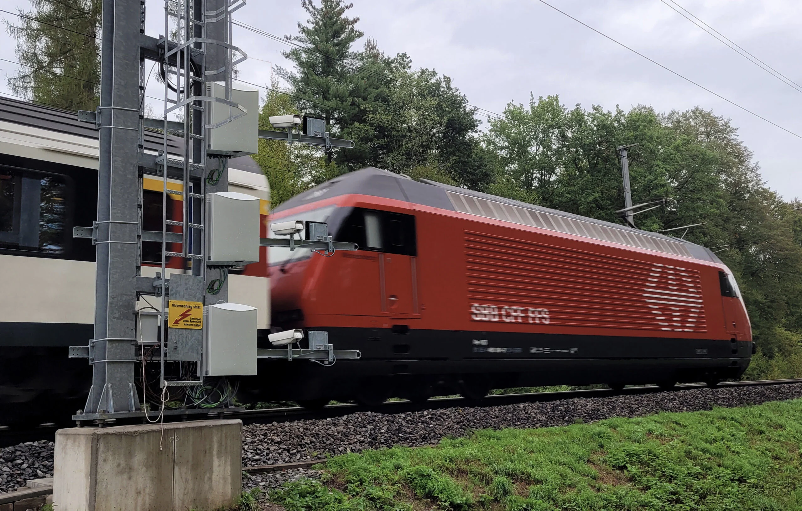 Eine rote Lokomotive und ein Personenzug fahren an einer Signalanlage vorbei, die auf Edge-Computing-Technologie basiert. Eine rote Lokomotive und ein Personenzug fahren an einer Signalanlage vorbei, die auf Edge-Computing-Technologie basiert.